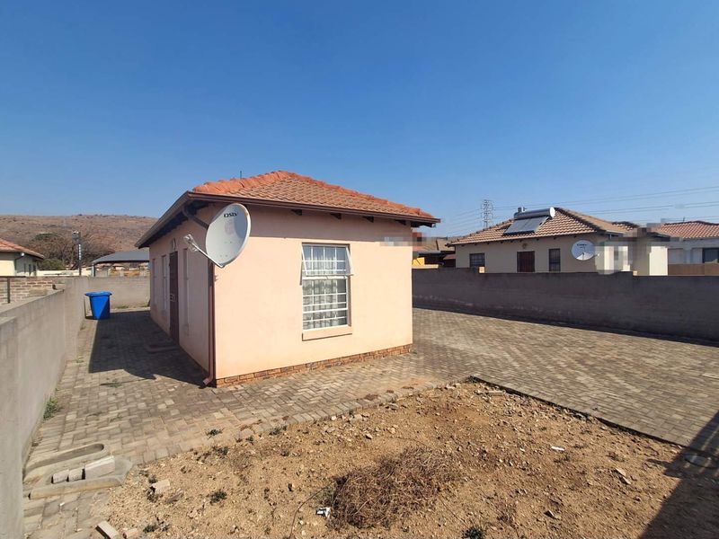 Rear view of a detached residential property featuring a tiled roof, paved driveway, and perimeter boundary walling.