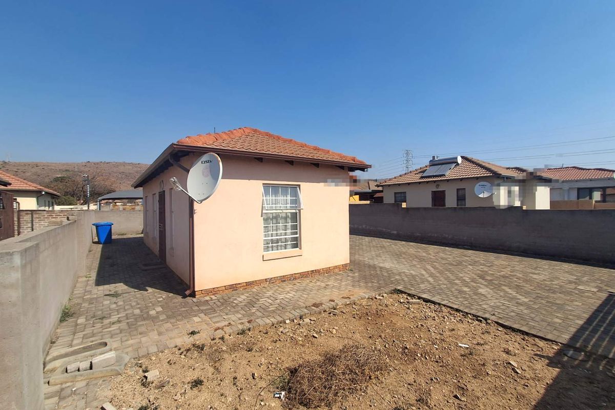 Rear view of a detached residential property featuring a tiled roof, paved driveway, and perimeter boundary walling.