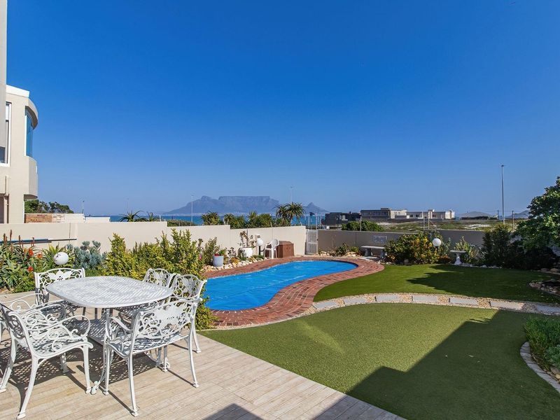 Outdoor entertainment area featuring a swimming pool, paved patio, and artificial lawn with scenic mountain and ocean views.