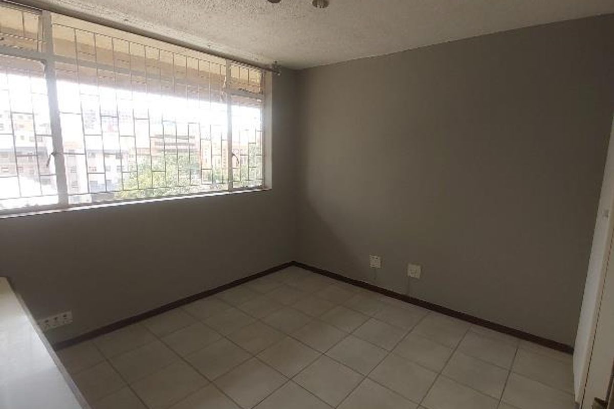 A vacant bedroom featuring neutral wall tones, tiled flooring, and large windows with security bars, offering a blank canvas for personalization.
