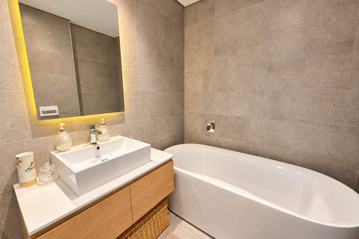 Modern bathroom featuring a sleek vessel sink on a wooden vanity, a freestanding bathtub, and elegant wall-mounted fixtures with ambient backlit mirror lighting.