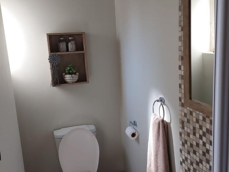 A compact guest bathroom featuring a modern vanity with a tiled splashback, a wall-mounted mirror, and a standard toilet.