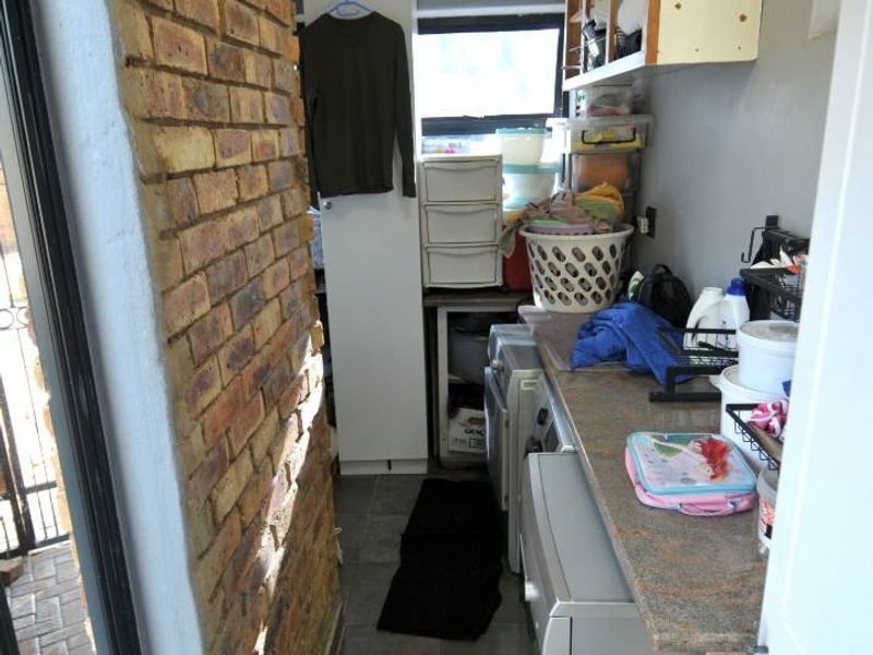 A functional laundry area featuring exposed brick walls, tiled flooring, laminate countertops, and wall-mounted storage cabinetry.