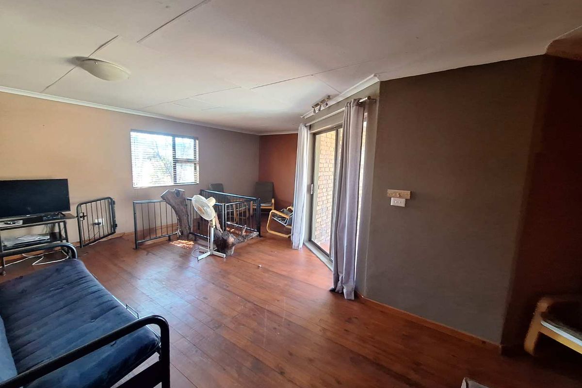 A living room featuring timber flooring, a sliding glass door leading to the exterior, and a metal safety railing.