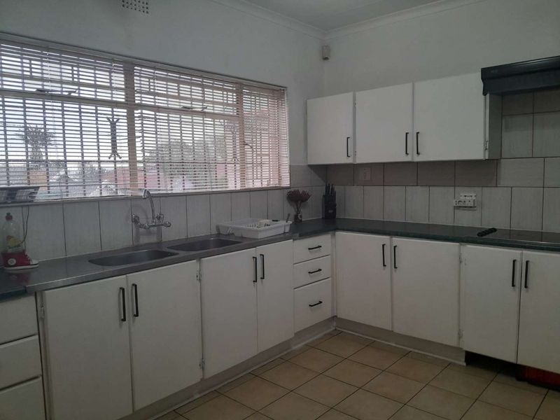 A functional kitchen featuring white cabinetry, laminate countertops, a double stainless steel sink, and tiled backsplash with neutral floor tiles.