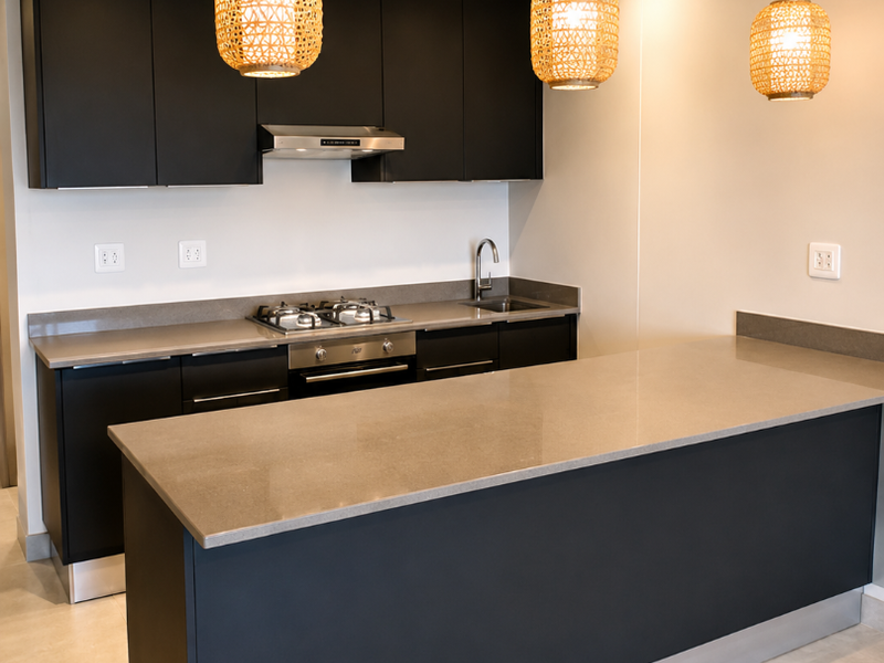 Modern kitchen featuring matte black cabinetry, stone countertops, integrated gas hob, oven, extractor fan, and a spacious breakfast island with pendant lighting.
