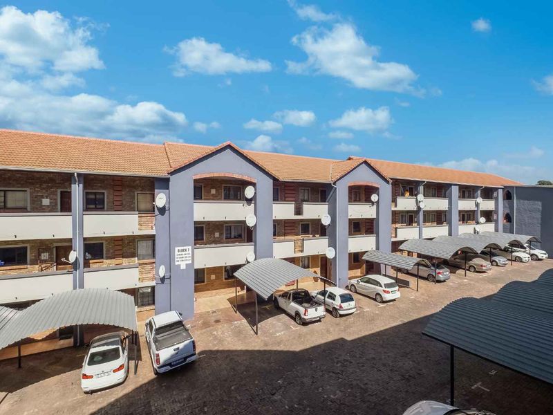 Exterior view of a multi-story apartment block featuring brick and painted facades, tiled roofing, and dedicated covered parking bays for residents.