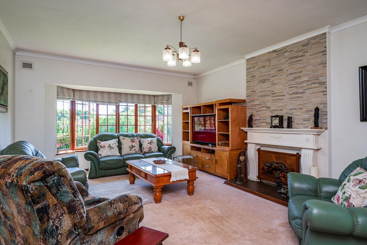 Spacious living room featuring a stone-clad fireplace, large bay window with garden views, and classic crown molding.