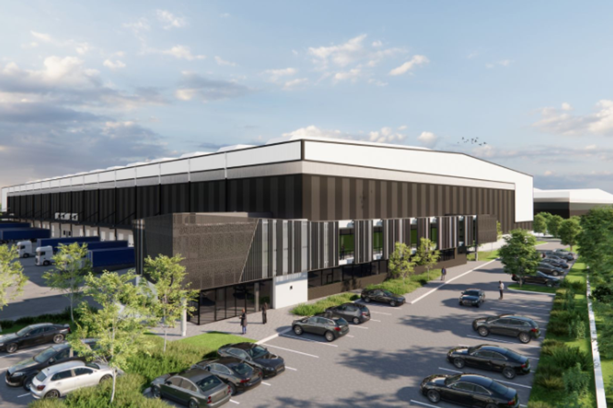 A modern industrial warehouse facility featuring extensive loading bays, a large asphalt parking area, and contemporary metal cladding with decorative architectural screening.