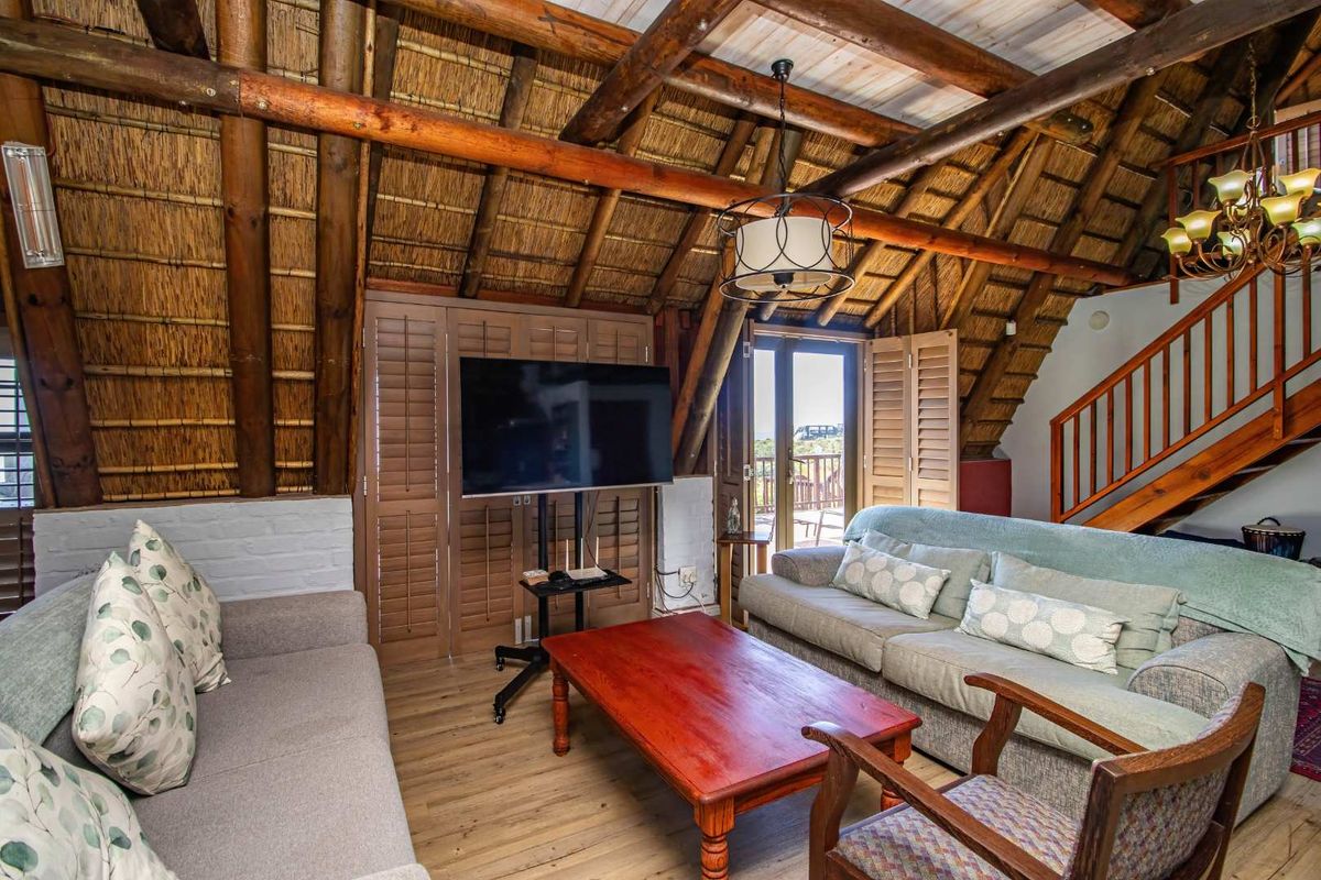 Cozy living room featuring a high vaulted thatched roof with exposed timber beams, wooden flooring, and direct access to an outdoor balcony.