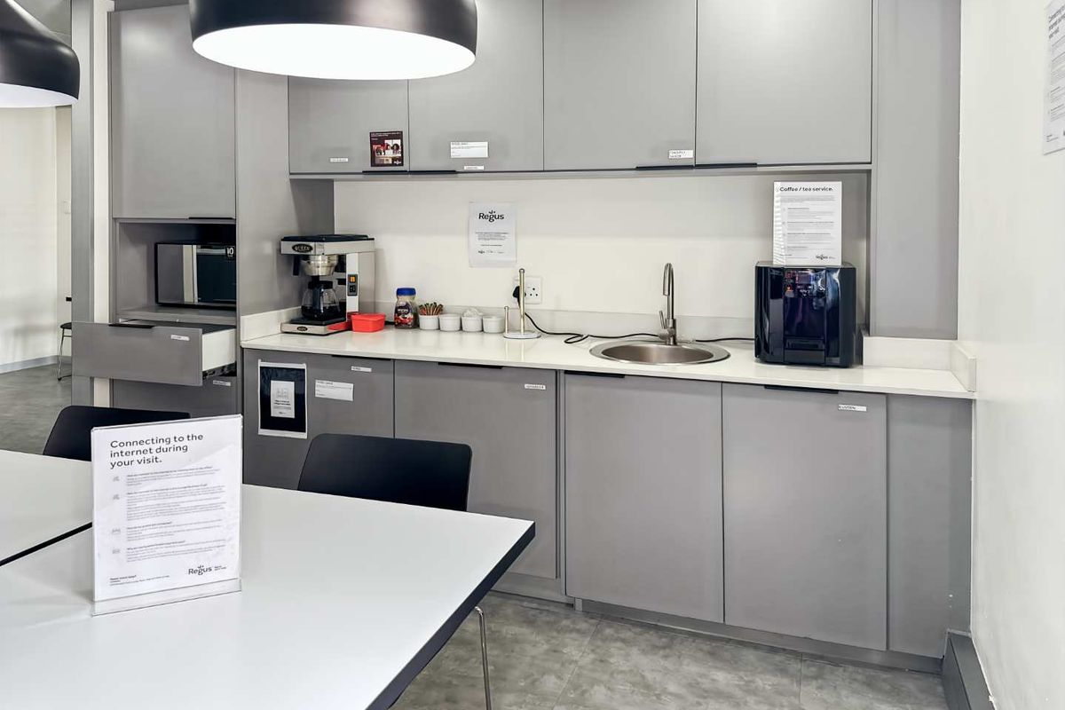 A modern office kitchenette featuring grey cabinetry, a stainless steel sink, and integrated storage space for office amenities.