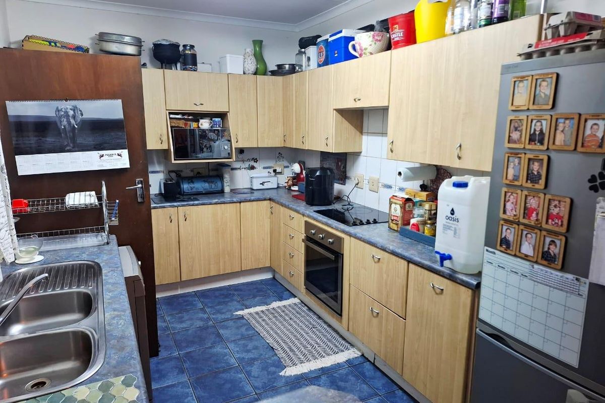 Functional kitchen featuring light wood-tone cabinetry, laminate countertops, a built-in oven with electric hob, and durable blue ceramic floor tiles.