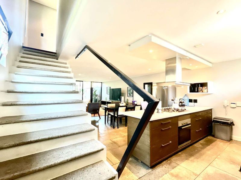 Modern open-plan living area featuring a contemporary kitchen with a central island, built-in appliances, and a striking staircase with a minimalist metal handrail.