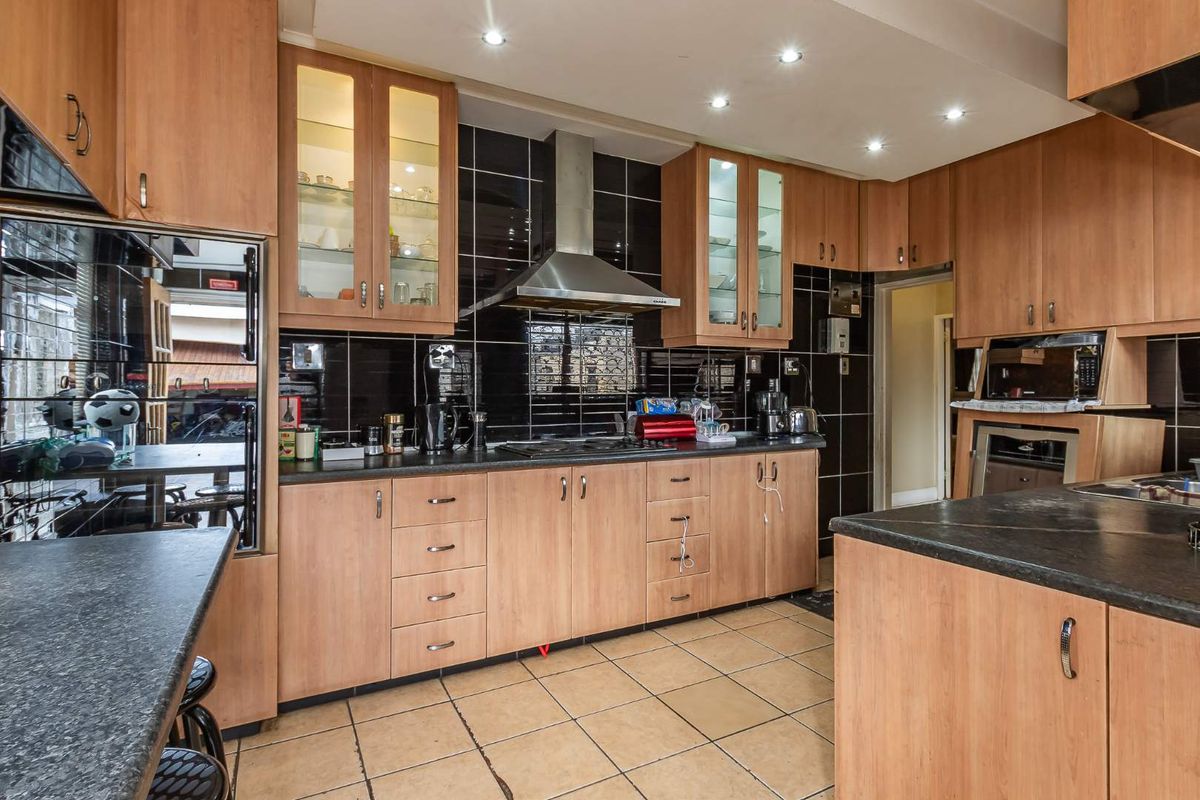 A functional kitchen featuring wood-finish cabinetry, black tiled splashbacks, a stainless steel extractor fan, and dark countertops with integrated storage.