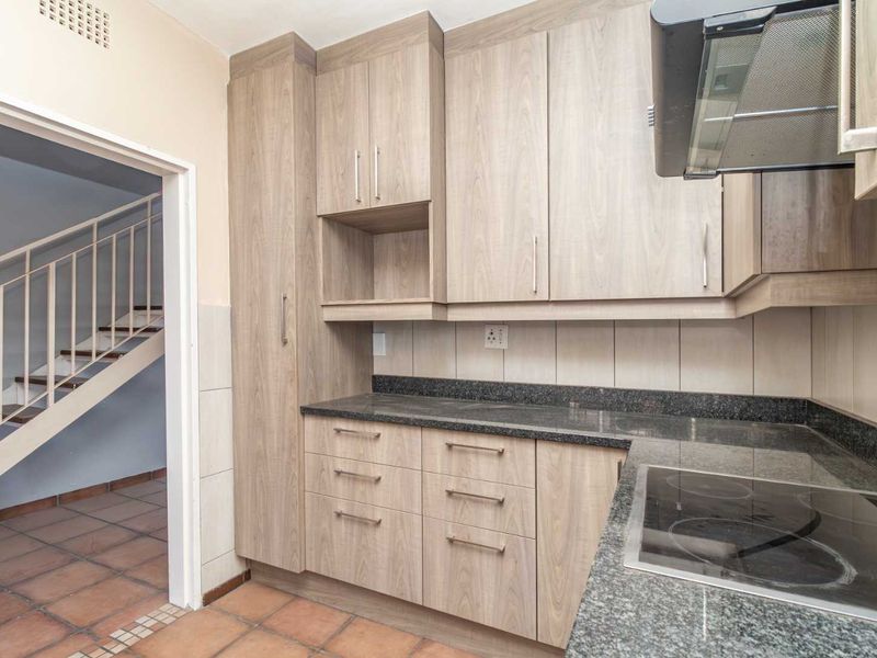 A functional kitchen featuring light wood-grain cabinetry, granite countertops, an integrated electric hob, and an extractor fan, with tiled flooring throughout.