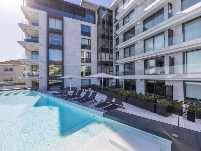 Modern apartment complex featuring a pristine swimming pool, stone-clad facade, and glass balcony balustrades, offering a sophisticated outdoor living space.