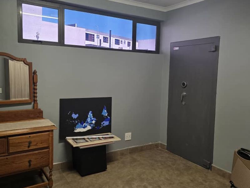 A bedroom featuring tiled flooring, a horizontal window, and a heavy-duty security door, providing a secure and functional living space.