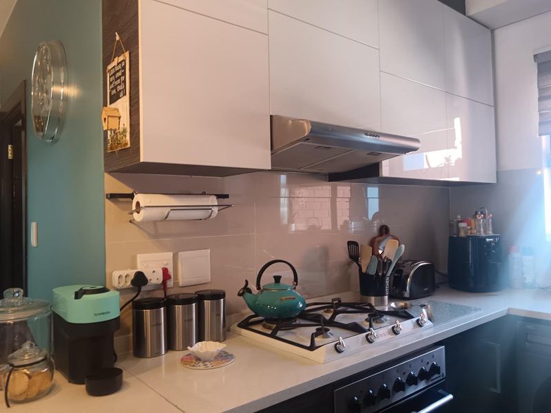 Modern kitchen featuring high-gloss cabinetry, stone countertops, a gas hob with extractor fan, and a tiled splashback.