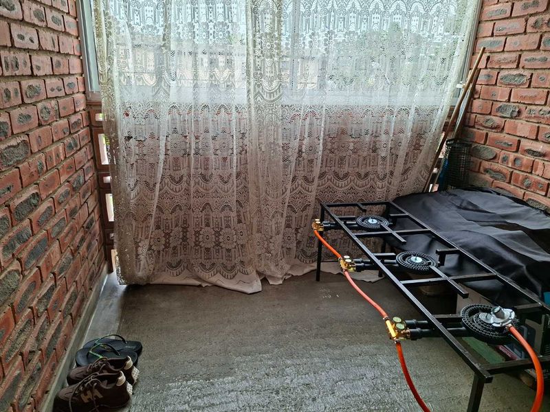 A covered balcony area featuring exposed brick walls, concrete flooring, and sliding glass windows, currently utilized as a utility and cooking space.