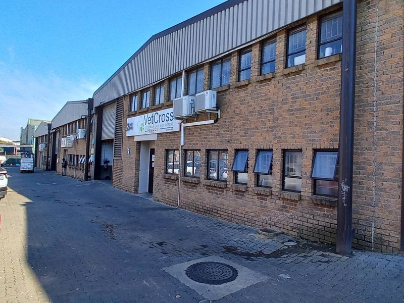 Exterior view of an industrial warehouse facility featuring face-brick facade, roller shutter doors, and multiple window units.