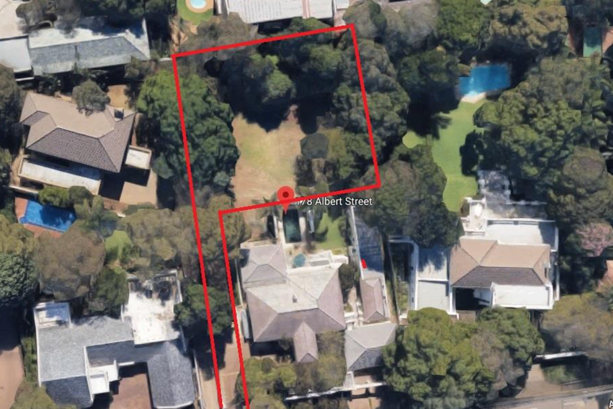 Aerial view of a residential vacant land plot featuring established trees and garden space, outlined in red for property identification.
