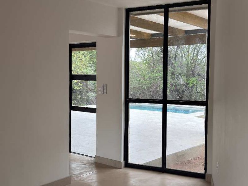 Bright, empty living space featuring polished concrete floors and large black-framed windows providing direct views of the outdoor pool area.