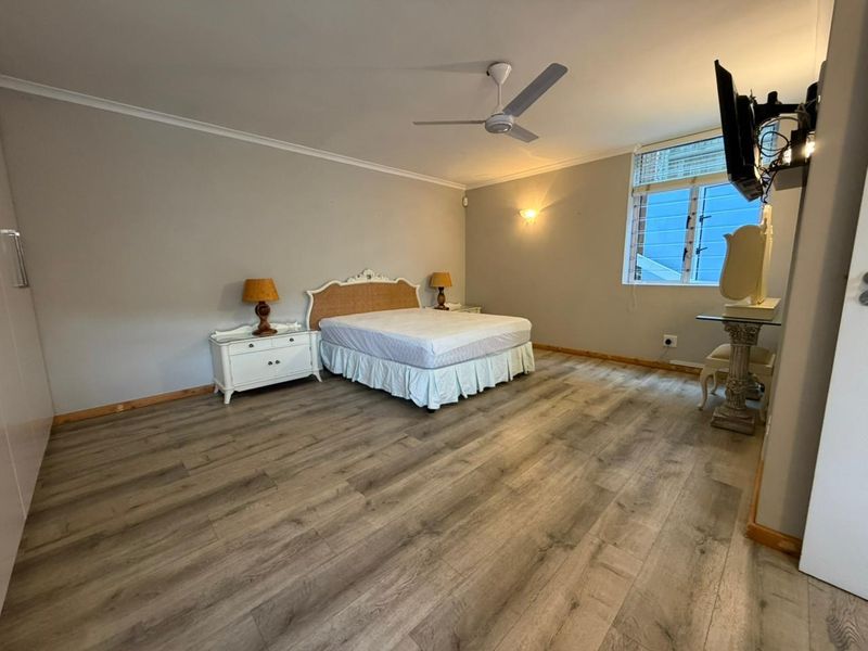 Spacious bedroom featuring durable laminate flooring, a ceiling fan, and a louvered window, offering a neutral canvas for personalization.