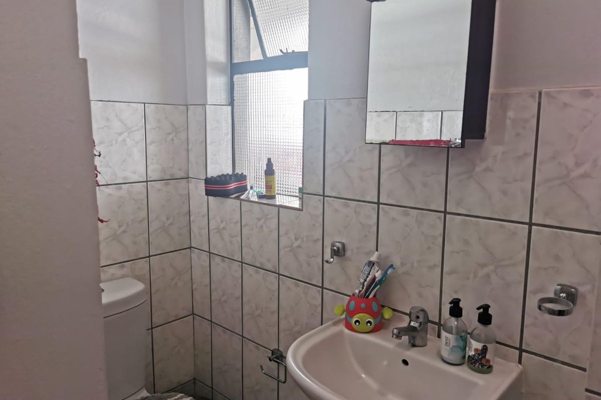 A functional bathroom featuring a wall-mounted basin, toilet, and a mirrored medicine cabinet with tiled walls and a privacy window.