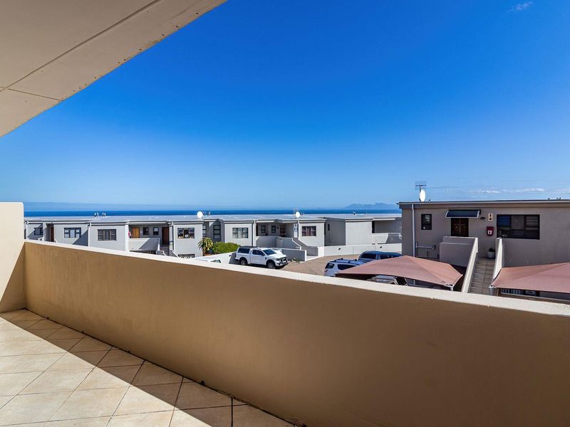 A spacious covered balcony featuring tiled flooring and a solid balustrade, offering clear views of the surrounding apartment complex and distant ocean.