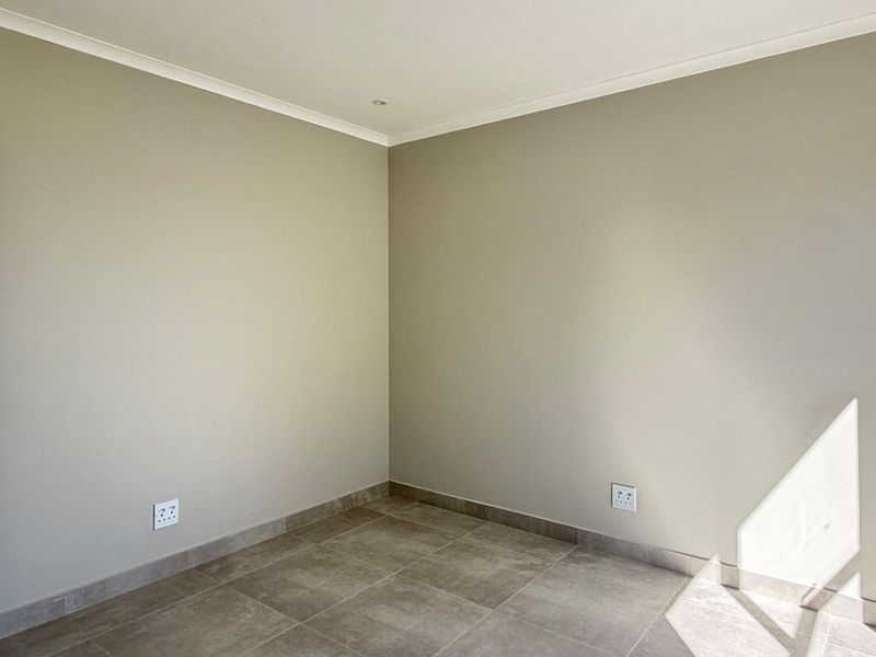 A clean, empty bedroom featuring neutral wall paint, tiled flooring, and modern electrical fixtures, ready for personalization.