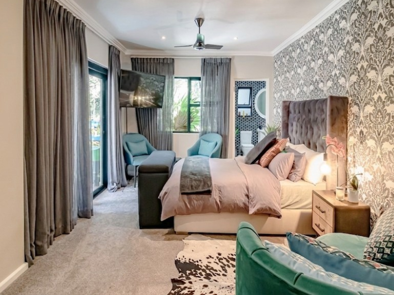 Spacious bedroom featuring patterned wallpaper, plush carpeting, a ceiling fan, and direct access to an outdoor area through sliding glass doors.