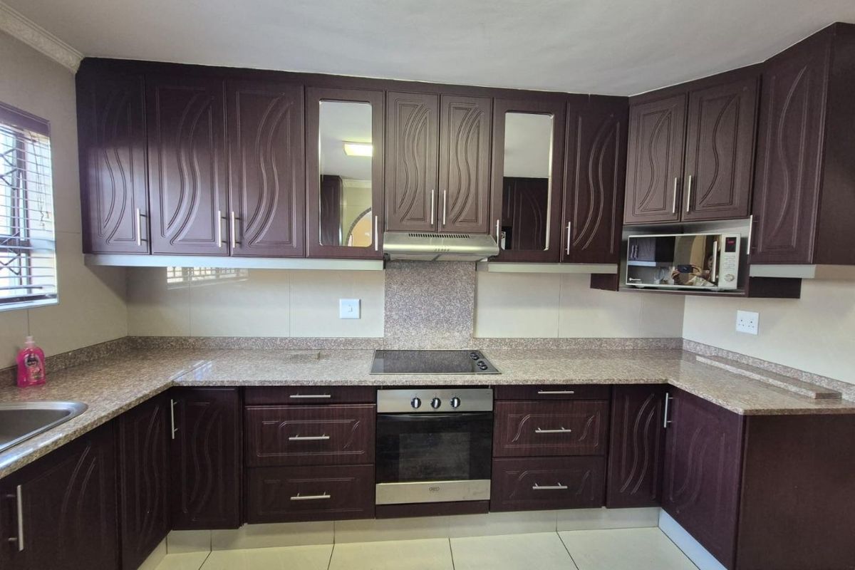 A functional kitchen featuring dark wood cabinetry, granite countertops, and integrated appliances including an oven, hob, and microwave.