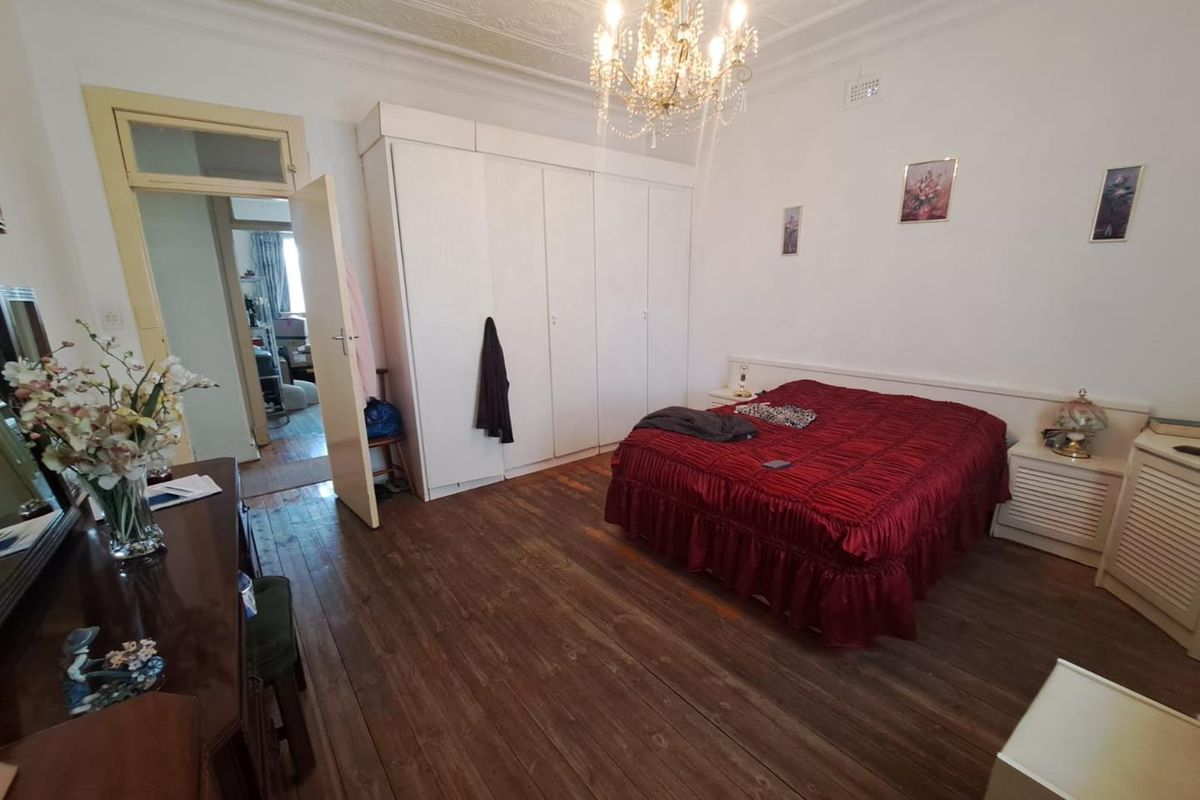 Spacious bedroom featuring original timber flooring, ornate ceiling detailing, built-in wardrobe storage, and a classic chandelier fixture.