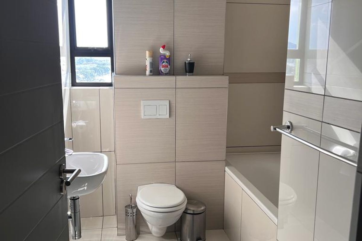 Modern bathroom featuring a wall-hung toilet with concealed cistern, pedestal washbasin, and a built-in bathtub with neutral floor-to-ceiling tiling.