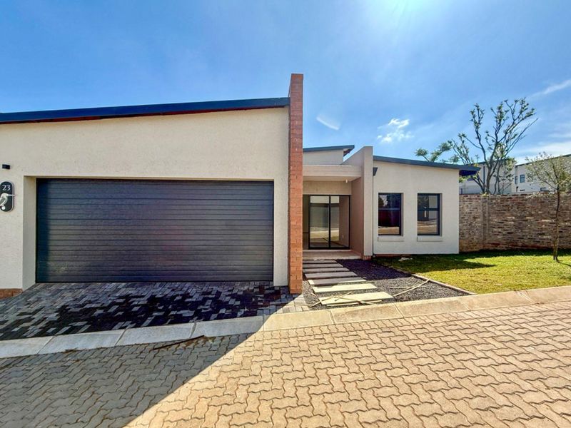 Modern cluster home exterior featuring a sleek automated garage door, paved driveway, and a contemporary entrance with a distinctive brick feature pillar.