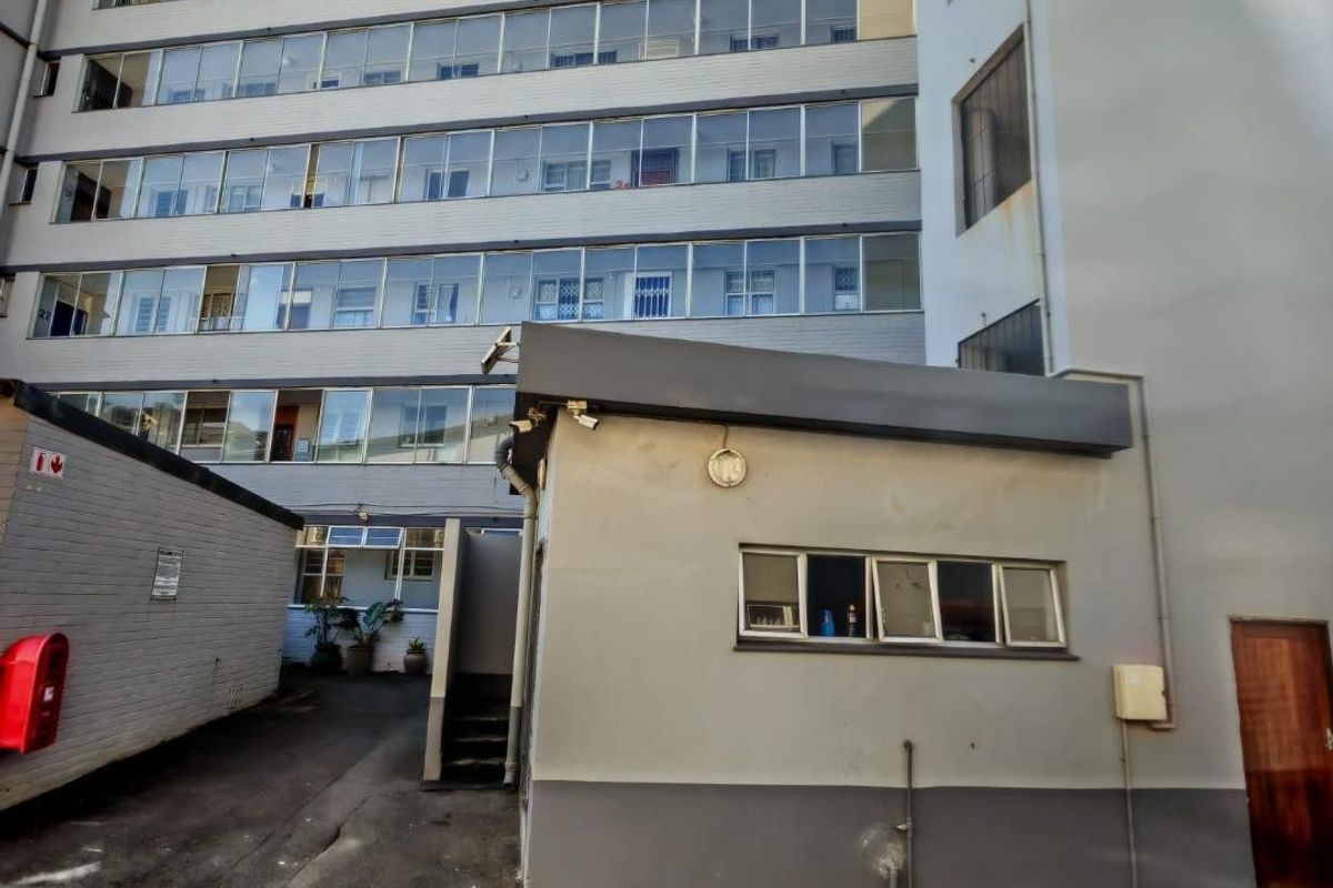 Exterior view of a multi-story apartment building showing the rear facade, utility structure, and paved driveway area.
