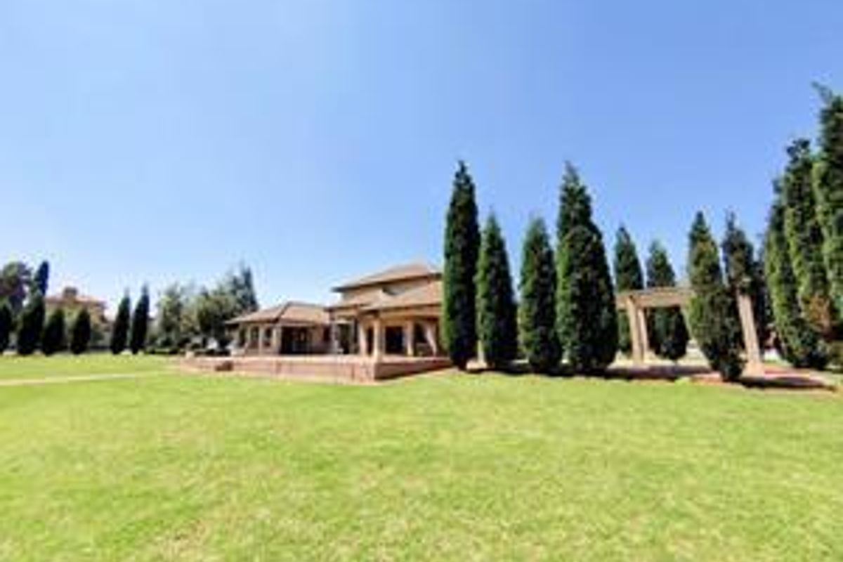 A spacious rear garden featuring a well-maintained lawn, mature cypress trees, and a covered patio area attached to the main building structure.