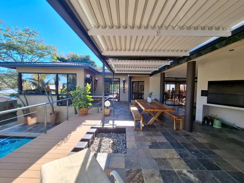 Spacious covered patio featuring a louvred roof, stone tile flooring, built-in fireplace, and direct access to a swimming pool with composite decking.