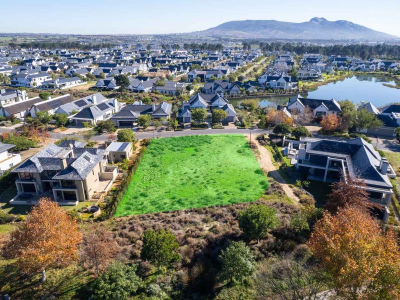 An aerial view of a vacant residential plot situated within a developed estate, surrounded by established homes and scenic landscape.