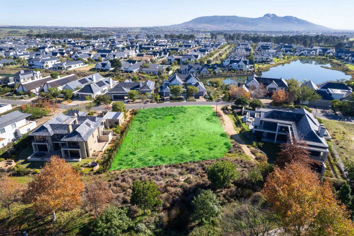 An aerial view of a vacant residential plot situated within a developed estate, surrounded by established homes and scenic landscape.