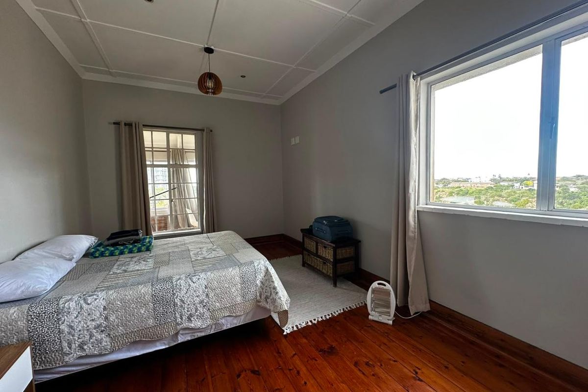 A bright bedroom featuring polished hardwood flooring, a decorative coffered ceiling, and large windows offering natural light and scenic views.