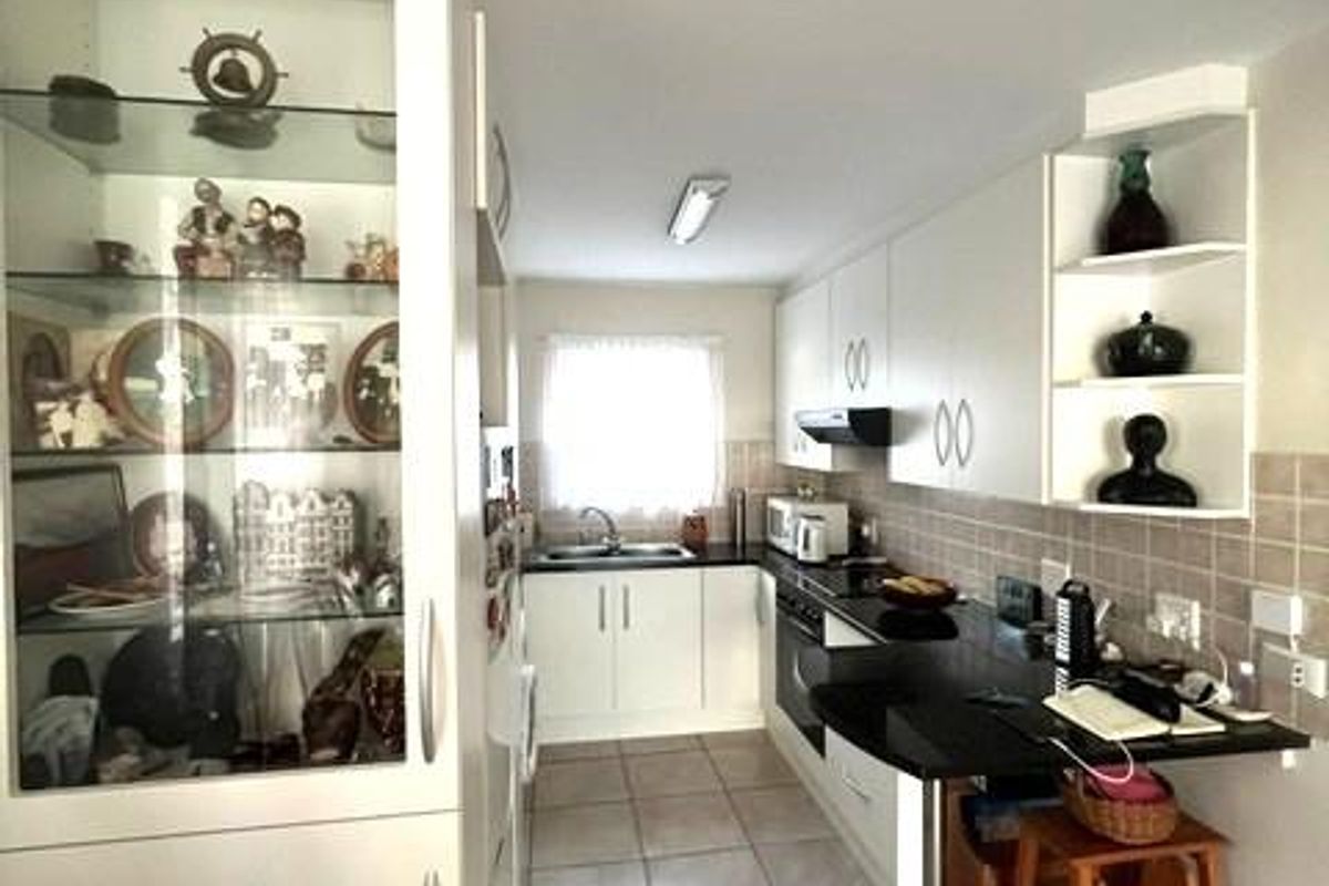 A functional kitchen featuring white cabinetry, dark countertops, tiled backsplash, and a built-in glass display cabinet, offering a clean and practical layout.