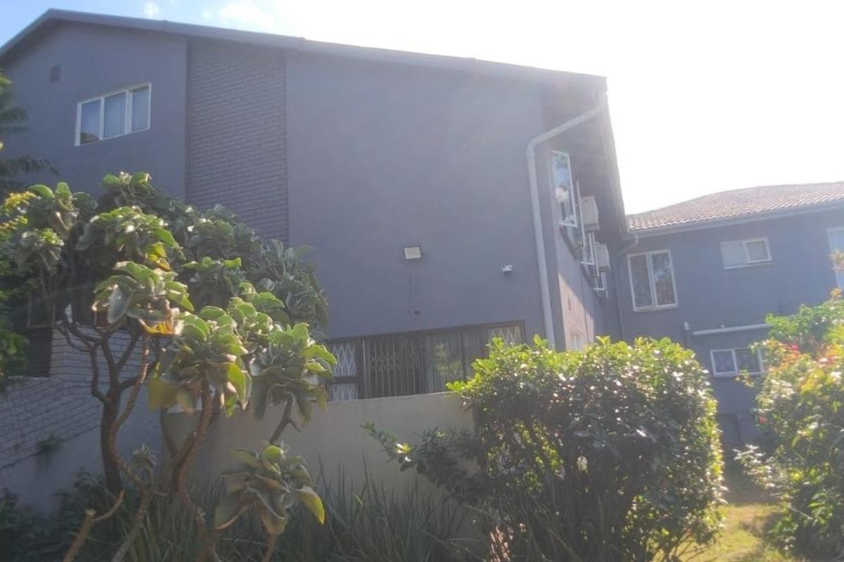 Rear elevation of the multi-story residential property featuring a grey rendered facade, tiled roofing, and established garden landscaping.