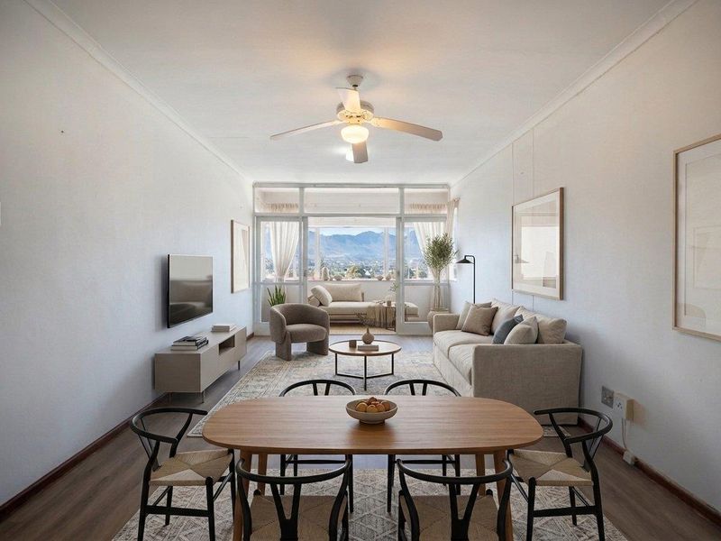 Bright open-plan living and dining area featuring laminate flooring, a ceiling fan, and large sliding doors leading to a balcony with mountain views.