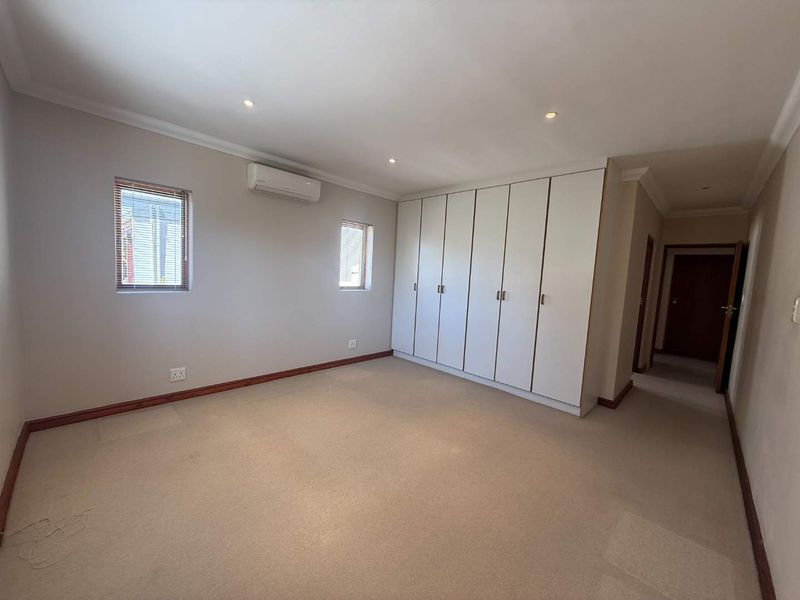 Spacious bedroom featuring neutral carpeting, extensive built-in storage cupboards, and a wall-mounted air conditioning unit.