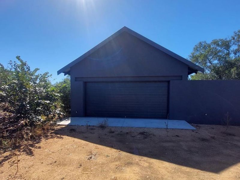 A modern dark-toned detached garage featuring a sectional door and a concrete apron, set within an unlandscaped plot.
