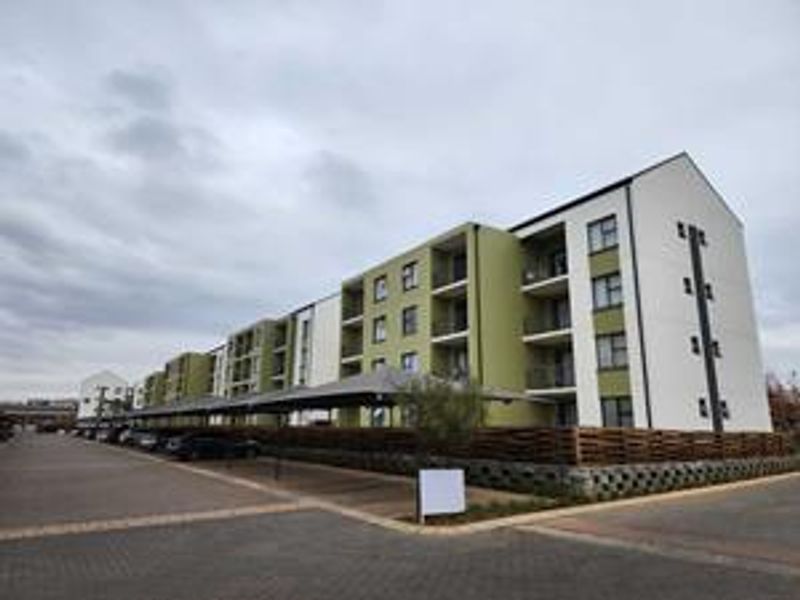 Exterior view of a modern multi-story apartment complex featuring covered parking bays, paved driveway, and private balconies.