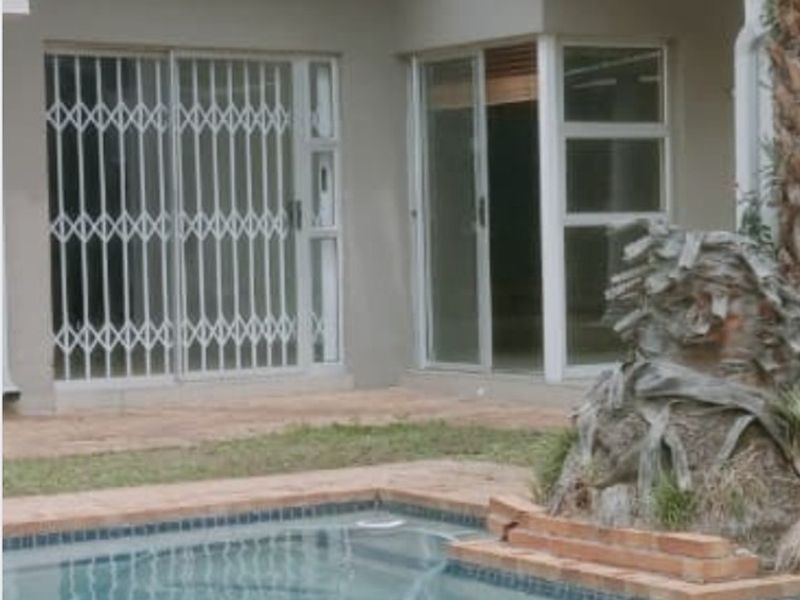 Rear exterior view featuring a swimming pool with brick coping, tiled roof, and sliding glass doors with security gates.