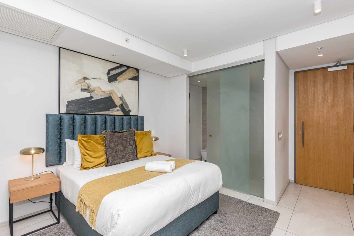 A modern bedroom featuring tiled flooring, recessed ceiling lighting, and a sleek frosted glass door leading to an en-suite bathroom.