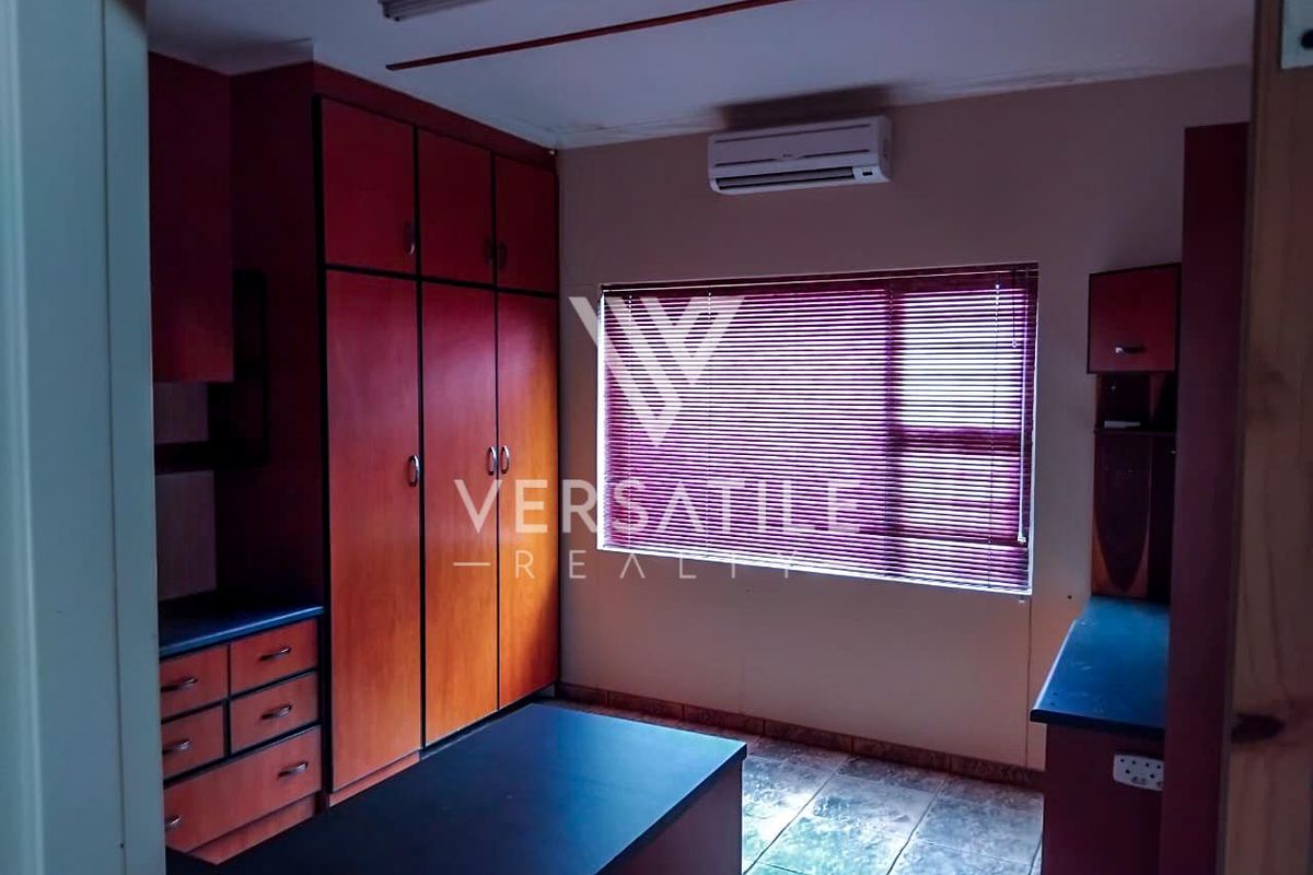 A functional bedroom or study featuring built-in wooden cabinetry, tiled flooring, a wall-mounted air conditioning unit, and window blinds.